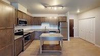 This single-floor residence offers a thoughtfully designed layout that balances open communal spaces with comfortable private retreats. The living area is bright and airy, finished with light-toned hardwood-style flooring and neutral walls, with a sliding glass door that opens to a private balcony overlooking the outdoors—bringing in generous natural light.

The kitchen is a standout feature, showcasing rich dark-stained cabinetry, light granite countertops, a classic white subway tile backsplash, and a full suite of stainless steel appliances including a range, microwave, refrigerator, and dishwasher. A center island with a matching granite surface provides additional prep and storage space, while track lighting overhead adds a modern touch.

The bedrooms are carpeted for comfort, each receiving natural light through window blinds. The primary bedroom includes a walk-in closet and convenient access to an in-unit laundry area. Two bathrooms serve the residence: one features a tub-shower combination with built-in shelving, while the other offers a walk-in shower, dark wood vanity with granite countertop, and tile flooring. Throughout the unit, a cohesive neutral color palette and consistent finishes create a clean, modern, and welcoming ambiance.