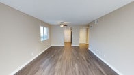 This single-floor space is designed with a clean, neutral aesthetic that carries throughout each room. The main living area is open and spacious, finished with durable wood-style plank flooring in a warm medium-tone that extends seamlessly through the common areas. Warm beige walls and crisp white baseboards create a cohesive backdrop, while a ceiling fan with an integrated light fixture provides both comfort and ambient lighting. A window fitted with horizontal blinds allows natural light to filter into the living space, enhancing the airy feel of the room. Visible HVAC vents are integrated into both the walls and floor, ensuring climate control throughout.

The galley-style kitchen is efficiently laid out, featuring white cabinetry on both sides complemented by dark granite-style countertops. Black appliances, including a coil-burner electric range, dishwasher, and refrigerator, provide a bold contrast to the white cabinetry. A tall, built-in pantry cabinet at the end of the kitchen offers generous additional storage. The same wood-style flooring continues into this space, maintaining visual consistency.

The bedroom is carpeted in a plush, light-toned carpet and features a textured ceiling. Full-length mirrored sliding closet doors line one wall, adding depth and reflecting natural light from the nearby window, contributing to a bright and functional sleeping space.