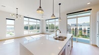 This contemporary single-floor residence is defined by clean lines, an abundance of natural light, and a thoughtfully designed open layout. Light hardwood flooring flows seamlessly throughout, complementing the crisp white walls and modern finishes found in every room.

The kitchen serves as the heart of the home, anchored by a large central island with a white quartz countertop and a double undermount sink. Pendant lighting hangs above, while white shaker-style cabinetry, a marble-effect tile backsplash, a stainless steel French door refrigerator, a built-in wall oven, a flush cooktop, and a sleek range hood complete the space. In-unit laundry is conveniently located just off the kitchen.

The open living area is bathed in natural light through expansive floor-to-ceiling windows that frame views of greenery and the surrounding neighborhood. A ceiling fan and stylish multi-bulb chandelier add character overhead. Sliding glass doors in the bedroom provide direct access to a private balcony, further enhancing the connection to the outdoors. Additional bedrooms feature oversized grid-pane windows that flood each room with sunlight.

The bathroom is finished with a white quartz vanity, an undermount sink, brushed nickel fixtures, and a tub-shower combination. A wide-angle entry hallway with recessed lighting leads seamlessly into the main living spaces, completing this bright and well-appointed residence.