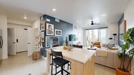 This single-story residence in San Diego, CA, 92154, offers a thoughtfully designed open-concept layout that seamlessly connects the kitchen, dining, and living areas. A bold teal accent wall serves as a unifying design element throughout the space, adding depth and a coastal character that complements the San Diego setting.

The kitchen is well-appointed with stainless steel appliances, including an electric range, built-in microwave, and refrigerator. Two-tone cabinetry pairs white upper cabinets with warm wood lower cabinets, complemented by a distinctive hexagonal blue tile backsplash and light countertops. A kitchen island with seating provides a casual dining option and connects to the open living area.

The living room is bright and welcoming, featuring a ceiling fan, recessed lighting, and a sliding glass door that opens to an outdoor space with palm tree views. The teal accent wall anchors the room, creating a relaxed, beachy ambiance.

The bedroom continues the coastal aesthetic with a tray ceiling, large windows with sheer curtains for natural light, and the signature teal accent wall. The single-floor layout ensures easy accessibility and a cohesive flow throughout the entire residence.