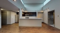 Located at 1211 Euclid Ave in Cleveland's vibrant midtown corridor, this single-floor residence showcases a thoughtfully designed open layout with striking architectural details throughout. The living area immediately impresses with dramatically tall ceilings and a skylight feature that floods the space with natural light, complemented by track lighting that runs along the upper perimeter for adjustable ambient illumination. Warm wood-style flooring extends throughout the main living areas, creating a cohesive and inviting atmosphere.

The kitchen serves as the central hub of the unit, featuring an extended peninsula with a light-toned stone countertop ideal for casual dining or food preparation. Dark espresso cabinetry reaches toward the upper walls, providing ample storage, while a classic white subway tile backsplash adds a clean contrast. Stainless steel appliances, including a refrigerator, range, and microwave, complete the modern setup.

Two bathrooms offer consistent finishes, each featuring dark vanity cabinetry with stone countertops and large mirrors. One bathroom includes a soaking tub and shower combination, while the second offers a walk-in glass-enclosed shower. The bedrooms are carpeted for comfort, with neutral tones and windows allowing natural light to enter. The overall design balances modern aesthetics with functional, everyday livability.