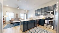 Located at 2422 S Carrier Pkwy in Grand Prairie, Texas, this well-appointed one-bedroom, one-bathroom unit offers a smart, efficient layout with modern design throughout. The open-concept kitchen and living area serves as the heart of the home, anchored by a striking kitchen featuring navy blue cabinetry, white subway tile backsplash, light quartz countertops, and stainless steel appliances. A central island with bar seating and pendant lighting above creates an inviting space for dining and entertaining. Light wood-style flooring flows throughout the main living areas, complementing the neutral walls and contributing to a bright, airy atmosphere. The living room benefits from multiple windows dressed with sheer curtains, allowing abundant natural light to fill the space. A hallway connects the main living area to the private bedroom, which is carpeted for comfort and features a window with outdoor views. The bedroom is served by a dedicated walk-in closet with built-in shelving and dual hanging rods, offering generous storage. The bathroom is conveniently positioned off the hallway, providing easy access from both the bedroom and living areas. Clean lines, contemporary finishes, and a cohesive neutral color palette give the entire unit a polished, modern feel.