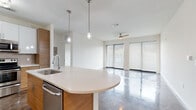 Located in the heart of Tampa's vibrant SoHo neighborhood, this single-floor residence showcases a thoughtfully designed modern interior with high-end finishes throughout. The open-concept living and kitchen area is anchored by gleaming polished concrete floors that reflect abundant natural light pouring in through large floor-to-ceiling windows fitted with sleek horizontal blinds. A ceiling fan adds comfort to the generous living space. The kitchen is a standout feature, boasting a combination of warm wood-grain and crisp white cabinetry, a neutral-toned quartz countertop island with an undermount sink, and a full suite of stainless steel appliances including a refrigerator, range, microwave, and dishwasher. A classic tile backsplash and pendant lighting complete the contemporary look. The bedrooms offer plush carpeted flooring, clean white walls, and dark-paneled doors, with one bedroom featuring a spacious walk-in closet outfitted with wire shelving for generous storage. The bathrooms are finished with light wood-look tile flooring and wood-grain vanities topped with quartz counters. One bathroom includes a soaking tub with shower combo, while another features a frameless glass walk-in shower, both finished in clean white tile.