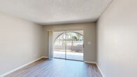 Located at 1400 Donegan Ave in Kissimmee, FL, this one-bedroom, one-bathroom residence offers a well-organized single-floor layout designed for comfortable everyday living. Light wood-style flooring runs throughout the unit, complemented by neutral gray walls and textured ceilings that create a clean, cohesive aesthetic.

The open-concept living and dining area is a standout feature, highlighted by a sliding glass door framed by a distinctive arched brick surround that leads to a private balcony. Natural light pours in through the glass door, brightening the space and offering views of the outdoor surroundings.

The kitchen is efficiently designed with gray upper cabinetry, white lower cabinets, stainless steel appliances including a range and refrigerator, and ample counter space. A separate pantry provides additional storage.

The bedroom is a comfortable, well-proportioned room with a window that lets in natural light and connects directly to a hallway featuring generous closet storage with louvered bi-fold doors. A utility room adds practical convenience to the layout.

The bathroom includes a full tub-shower combination with white tile surround. A hallway and additional closet space round out this efficiently planned residence, ideal for those seeking a streamlined living environment in central Kissimmee.