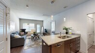 Located at 20233 E 45th St in Independence, Missouri, this single-floor residence offers a thoughtfully designed open-concept layout with modern finishes. The kitchen serves as a central focal point, featuring dark espresso cabinetry, light countertops, a tiled backsplash, and a full suite of stainless steel appliances including a refrigerator, electric range, and built-in microwave. A kitchen island with an undermount double sink and pendant lighting provides both additional prep space and casual seating. Wood-style flooring runs throughout the main living areas, adding warmth and continuity.

The living area is generously sized and filled with natural light from multiple windows, creating a bright and welcoming atmosphere. A private exterior door opens directly from the living space, enhancing accessibility and airflow. Both bedrooms feature plush carpeting, ceiling fans, and wide windows that invite natural light. The primary bathroom is well-appointed with a dual-sink vanity topped with light countertops, dark cabinetry with chrome hardware, a large wall mirror illuminated by a multi-bulb light bar, and a tub-shower combination. The overall design balances contemporary style with functional comfort throughout.