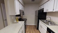 This single-story residence at Canter Chase offers a well-organized layout with distinct living, sleeping, and functional zones. The galley-style kitchen is efficiently designed with white cabinetry lining both sides, speckled light countertops, and stainless steel appliances including an electric range, over-the-range microwave, and refrigerator. Wood-look flooring runs throughout the kitchen, adding warmth to the space.

The living area is generously sized, featuring plush carpeting, a textured ceiling, and a ceiling fan with integrated lighting. A wood-burning fireplace serves as a focal point, flanked by a window that allows natural light to filter in. The layout offers an open sightline toward the kitchen, enhanced by a pass-through view and a chandelier that adds a decorative touch to the transitional dining area.

The bedroom is a comfortable, carpeted room with a large window dressed with blinds, providing natural light and outdoor views. The bathroom is clean and functional, featuring a tub-shower combination, a white vanity with speckled countertop, and wood-look flooring that ties cohesively to the rest of the unit. Overall, the space presents a practical and livable design throughout.