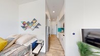 This efficiently designed one-bedroom, one-bathroom unit makes excellent use of its compact footprint across a single floor. The layout flows logically from the entrance through a narrow hallway that connects all key areas of the unit. Light wood-tone flooring runs throughout, lending warmth and visual continuity to the space.

The kitchen is a standout feature, boasting crisp white cabinetry with brushed silver hardware, light quartz countertops, and a striking teal ceramic tile backsplash that adds a bold pop of color. Stainless steel appliances, including a refrigerator and over-range microwave, complete the functional cooking area. Recessed lighting keeps the space bright and modern.

The bedroom is a cozy, well-defined retreat featuring a window that invites natural light and offers an outdoor view. White walls provide a clean backdrop, complemented by tasteful decor. A smart thermostat is mounted on the wall, reflecting the unit's modern conveniences.

The bathroom maintains the clean, minimalist aesthetic with white walls, wood-look flooring, a shower-tub combination with a curtain enclosure, and a glass shelf for storage.

Throughout the unit, the design emphasizes clean lines, neutral tones accented with color, and smart use of every square foot, making it a practical and stylish living space.