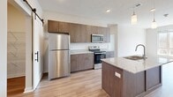 This single-floor residence features a thoughtfully designed open-concept layout that connects the kitchen and living room, creating a cohesive and functional central living space. The kitchen is a standout area, equipped with stainless steel appliances including a refrigerator, electric range, and microwave. Warm-toned flat-front cabinetry extends to the ceiling, providing ample storage, while granite countertops continue across a substantial central island fitted with a dual-basin sink and pendant lighting above. A sliding barn door leads to a dedicated pantry with built-in shelving, adding practical storage. Light wood-tone flooring flows throughout the main living areas, complemented by neutral white walls that enhance the bright, airy atmosphere. Large windows in the living area and primary bedroom frame natural views of surrounding greenery. The bedrooms include carpet flooring; secondary bedrooms feature ceiling fans and window treatments. The bathrooms display granite-topped vanities and wood-tone cabinetry consistent with the overall design palette. A dedicated laundry room accommodates a full-size washer and dryer. Two closets and a hallway complete the efficient floor plan.