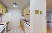 Located on 84 Avenue NW in Edmonton, Alberta, this one-bedroom, one-bathroom unit offers a practical and well-organized layout across a single floor. Light-toned hardwood flooring runs throughout the main living areas and bedroom, lending a clean, cohesive look to the space. The living room is bright and open, benefiting from a large window fitted with blinds that allows natural light to fill the room, while baseboard heating ensures year-round comfort. A pass-through counter connects the living area to the galley-style kitchen, which features light wood cabinetry, laminate countertops, tile flooring, and white appliances including a refrigerator, electric range, and dishwasher. The bedroom is a comfortable size, complete with a sliding-door closet offering built-in shelving for organized storage, and a window with views of the surrounding Edmonton skyline. The bathroom is finished with large-format ceramic wall tiles surrounding a full soaker tub, complemented by tile flooring. A hallway with an intercom panel connects the rooms efficiently. Textured ceilings are present throughout, adding a classic character to the unit's clean, neutral interior palette.