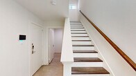 Located in the vibrant Uptown neighborhood of Dallas, TX, this modern three-story home offers a clean, contemporary design with thoughtful details across every level. The entry level welcomes residents through a crisp white entrance foyer, featuring dark-stained hardwood stair treads against white risers — a striking visual contrast that sets the tone for the home's aesthetic. The main living level is bright and open, combining the kitchen and living areas into one cohesive space. The kitchen is appointed with white shaker cabinetry, quartz countertops, stainless steel appliances including a French door refrigerator, and an island with an undermount sink. Wide-plank hardwood flooring and abundant natural light from multiple windows and a sliding glass door leading to a private balcony give this level an airy, spacious feel. A sleek powder bathroom with a vessel sink adds a modern touch. The upper floor houses the two bedrooms, each featuring plush carpet flooring and generous windows. The primary bedroom benefits from elevated ceilings and a walk-in closet with built-in shelving. The five bathrooms throughout feature tile flooring, white vanities, and clean modern fixtures. The overall palette of white walls and natural wood tones creates a bright, cohesive ambiance throughout the home.