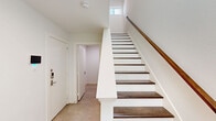 Located in the vibrant Uptown neighborhood of Dallas, TX, this modern three-story home offers a clean, contemporary design with thoughtful details across every level. The entry level welcomes residents through a crisp white entrance foyer, featuring dark-stained hardwood stair treads against white risers — a striking visual contrast that sets the tone for the home's aesthetic. The main living level is bright and open, combining the kitchen and living areas into one cohesive space. The kitchen is appointed with white shaker cabinetry, quartz countertops, stainless steel appliances including a French door refrigerator, and an island with an undermount sink. Wide-plank hardwood flooring and abundant natural light from multiple windows and a sliding glass door leading to a private balcony give this level an airy, spacious feel. A sleek powder bathroom with a vessel sink adds a modern touch. The upper floor houses the two bedrooms, each featuring plush carpet flooring and generous windows. The primary bedroom benefits from elevated ceilings and a walk-in closet with built-in shelving. The five bathrooms throughout feature tile flooring, white vanities, and clean modern fixtures. The overall palette of white walls and natural wood tones creates a bright, cohesive ambiance throughout the home.