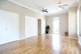 Located at 4129 Inverness Road in Virginia Beach, Virginia, this single-floor space offers a clean, welcoming layout designed for functional commercial use. The entryway sets the tone with natural stone-look tile flooring in warm, earthy tones that carries throughout the space, providing both durability and visual appeal. Large glass panel doors at the entry allow an abundance of natural light to flow in, offering a clear view into the adjacent sunlit interior area, which features ceiling fans, additional tile flooring, and casual furnishings that suggest a comfortable gathering or reception space. The warm cream-toned walls are accented with tasteful nautical-themed artwork, including a framed photograph of a sailboat on calm waters — a fitting nod to the coastal Virginia Beach setting. The corridor provides access to clearly marked men's and women's restrooms, both equipped with paneled white doors that complement the clean, neutral aesthetic of the space. A fire alarm pull station is prominently installed in the hallway, reflecting attention to safety compliance. The overall ambiance is bright, tidy, and inviting, with a coastal-inspired character suited to a professional or community-oriented environment.