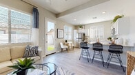 This single-story home offers a cohesive, modern design with a neutral color palette, light wood-look flooring, and an abundance of natural light throughout. The open-concept layout connects the living room, dining area, and kitchen seamlessly, creating a comfortable and functional flow.

The living room features a soft sectional sofa, a glass-top coffee table, and large framed abstract artwork, anchored by a plush area rug. Adjacent to the living area is a cozy dining nook with a round table, seating for two, and a glass door opening directly to the outdoor patio. The kitchen is well-appointed with crisp white shaker cabinetry, light quartz countertops, stainless steel appliances including a range, over-the-range microwave, and refrigerator. A peninsula with bar seating provides additional dining and prep space.

The bedrooms are bright and inviting, each featuring large windows with blinds and drapes that allow for generous natural light and outdoor views. The primary bathroom is a standout feature, offering a spacious layout with a dual-sink vanity, a glass-enclosed shower, wood-look tile flooring, and direct access to a walk-in closet. A private water closet provides added functionality. The home's consistent finishes and thoughtful design make it a polished, move-in-ready space.