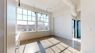 Located in St. Louis, MO, this two-bedroom, one-bathroom loft on Locust Street delivers an urban industrial aesthetic with thoughtful modern updates. The open-plan living and kitchen area is anchored by floor-to-ceiling grid windows that flood the space with natural light and frame sweeping city views. Polished concrete floors run throughout, complementing the loft's industrial character, while soaring ceilings create an airy, expansive feel well beyond the unit's modest footprint. The kitchen features sleek light-wood cabinetry, stainless steel appliances including a built-in oven and microwave, and a clean countertop workspace beneath a striking black track lighting system. A standout design element is the oversized frosted sliding glass partition, which separates spaces with a contemporary flair. The primary bedroom benefits from large windows overlooking the surrounding cityscape. The bathroom continues the modern industrial theme with dark accent walls, a glass-enclosed shower, and wall-mounted fixtures. A hallway connects the rooms efficiently, maximizing the use of the overall layout. This loft combines raw architectural character with refined finishes, making it a compelling urban living space in the heart of St. Louis.