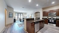 Located at 1200 S Conkling St in Baltimore's vibrant Canton neighborhood, this modern single-floor apartment offers 1,090 square feet of thoughtfully designed living space with 2 bedrooms and 5 bathrooms. The open-concept kitchen and living area serves as the heart of the unit, featuring rich dark wood cabinetry, granite countertops, stainless steel appliances, a built-in wine rack, and a peninsula island with bar seating. Arched architectural details add character to the kitchen-dining transition. The living room is bright and welcoming, anchored by large windows that frame urban views and flood the space with natural light. Luxury vinyl plank flooring runs throughout the entire unit, providing a clean, cohesive aesthetic. Both bedrooms are generously sized, each equipped with ceiling fans and large windows. The primary bedroom measures 180 square feet and connects to a spa-inspired en-suite bathroom featuring dual vanities, slate tile accents, a soaking tub, and a walk-in closet with multi-tier wire shelving. Additional bathrooms continue the upscale tile and hardwood aesthetic. A connecting hallway ties all spaces together efficiently. This well-appointed residence combines contemporary design with functional layouts ideal for modern urban living.