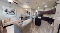 Located at 11206 University in Lubbock, Texas, this single-story home offers an open-concept design that seamlessly connects the living, dining, and kitchen areas into one cohesive and functional space. The living room features warm neutral tones, a ceiling fan, and an elegant chandelier, creating a comfortable and welcoming atmosphere. Wood-look plank flooring extends throughout the main living areas, adding warmth and a sense of continuity to the layout. The kitchen is a standout feature, showcasing rich dark cabinetry, light stone countertops, a breakfast bar with barstool seating, pendant lighting, and black appliances. It is well-equipped and designed with both style and practicality in mind. Adjacent to the kitchen, a cozy dining area provides an intimate space for everyday meals, accented by decorative wall pieces that add character to the interior. The vaulted ceiling in the main living area enhances the sense of openness and airiness throughout the home. Neutral wall tones and thoughtful lighting choices contribute to a clean, modern aesthetic. The single-floor layout ensures ease of navigation throughout the home, making it both accessible and efficient. Overall, the space offers a balanced combination of contemporary design and everyday comfort.