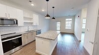 This contemporary 730 square foot apartment in Kingston, MA offers a well-designed living space on a single floor. The open concept layout maximizes the use of space, creating a seamless flow between the living areas. The kitchen is a standout feature, boasting white cabinetry, granite countertops, and stainless steel appliances. Two pendant lights over the kitchen island add a touch of modern elegance.

The spacious primary bedroom, measuring 170 square feet, is equipped with a ceiling fan and large windows that allow ample natural light. The bathroom is sleek and functional, featuring a tiled shower, granite vanity, and modern fixtures. Wood-look flooring runs throughout the apartment, adding warmth and continuity to the space.

Storage solutions include a closet with wire shelving, providing practical organization options. The living area is bright and airy, with windows offering views of the surrounding area. Recessed lighting and additional ceiling fans contribute to the overall modern aesthetic and comfort of the space.

Located at 1 Kingston Collection Way, this apartment combines style and functionality in a compact yet well-appointed living environment, ideal for those seeking a contemporary urban lifestyle.