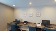 This single-floor business center is designed to provide a functional and focused environment for work and productivity. The room features a continuous marble-patterned countertop running along the wall, offering ample workspace for multiple users simultaneously. Equipped with desktop computers, keyboards, and both laser and inkjet printers, the space is fully outfitted to handle a range of professional tasks including printing, scanning, and general computing needs. Comfortable blue upholstered chairs are positioned at each workstation, providing ergonomic seating for extended use. The walls are finished in a clean, neutral tone, lending the space a calm and professional atmosphere. Recessed ceiling lighting ensures consistent illumination throughout, while a window fitted with white horizontal blinds allows for natural light control and contributes to a bright, pleasant working environment. A ceiling-mounted HVAC vent ensures comfortable climate control year-round. The walls are accented with a trio of matching framed artwork featuring circular botanical motifs, adding a subtle decorative touch that softens the utilitarian nature of the space. Overall, this business center strikes a balance between practicality and comfort, making it a well-appointed destination for focused work.