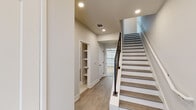Located at 3706 Governors Dr SW in Huntsville, Alabama, this contemporary three-floor home showcases clean architectural lines and modern finishes throughout. Light wood-tone flooring flows across the main level, anchoring an open-concept layout that connects the living area and kitchen seamlessly. The living room features a sleek built-in fireplace framed by custom shelving, large windows that invite natural light, and a ceiling fan overhead. The kitchen is well-appointed with gray shaker-style cabinetry, stainless steel appliances, a subway tile backsplash, and a central island with a white countertop and pendant lighting above. A powder room on the main level features a blue-gray vanity, white countertop, and a large framed mirror. The staircase, finished with wood-tone treads, white risers, and matte black metal balusters, connects all three floors with modern style. A full bathroom on an upper floor includes tile flooring, a tub-shower combination, and a vanity with matte black hardware. The attached garage offers generous space with concrete flooring and a panel-style garage door with an automatic opener. Built-in shelving and thoughtful storage spaces are found throughout, contributing to a well-organized and functional home.