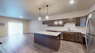 Located at 3704 42nd St S in Fargo, North Dakota, this 1-bedroom, 1-bathroom unit offers a thoughtfully designed single-floor layout that maximizes functionality and comfort. The open-concept kitchen and living area serves as the heart of the home, showcasing rich dark-stained cabinetry, light quartz countertops, and a central island illuminated by two stylish pendant lights. Stainless steel appliances, including a refrigerator, range, and microwave, complete the kitchen. Durable wood-look flooring runs throughout the main living areas, adding warmth and visual continuity. A sliding glass door in the living area allows for natural light and outdoor access. The spacious bedroom features soft carpeting, a large window for natural light, and baseboard heating. The full bathroom is finished with matching dark cabinetry, a quartz vanity, wood-look vinyl flooring, and a tub-shower combination. Throughout the unit, neutral warm tones on the walls create a clean, inviting atmosphere. Baseboard heating is present throughout, ensuring comfort during Fargo's colder months. The overall design strikes a balance between modern aesthetics and practical, everyday livability.