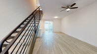 This well-appointed two-story home showcases a clean, modern design with a bright and cohesive aesthetic throughout. The main level features light wood-look tile flooring that flows seamlessly from the open living area into the kitchen. The living room is generously sized, highlighted by a ceiling fan and access to an outdoor area through sliding glass doors fitted with vertical blinds, inviting natural light into the space.

The kitchen is a standout feature, offering white shaker-style cabinetry, light quartz countertops, a peninsula with an integrated sink, and a full suite of stainless steel appliances including a refrigerator, electric range, microwave, and dishwasher. Recessed lighting illuminates the space effectively. A powder bathroom on the main level features a white vanity with brushed gold fixtures and matching hardware.

Upstairs, the bedrooms are carpeted for comfort, with windows providing natural light and ample wall space for flexible furnishing. A full bathroom on the upper level includes a tub-shower combination with white tile surround, a white vanity, and brushed gold fixtures consistent with the home's design language. A staircase with a modern metal railing connects the two levels, adding an architectural detail that complements the home's contemporary style throughout.