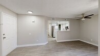 This single-floor residence offers a clean, modern aesthetic throughout, characterized by neutral warm-gray walls, light wood-look flooring, and textured ceilings that tie the space together cohesively. The open-concept layout connects the living area to the kitchen seamlessly, making the space feel airy and functional. The living area is generously proportioned, featuring a ceiling fan, a sliding glass door with vertical blinds that invites natural light, and a bright window that further illuminates the room. The kitchen is well-appointed with white cabinetry, light stone-look countertops, and stainless steel appliances including a refrigerator, electric range, and over-the-range microwave. A peninsula with a double stainless steel sink and additional counter space provides both extra prep area and a natural divide between the kitchen and living spaces. A skylight above the kitchen enhances the brightness of the cooking area. The bedroom is a comfortable, light-filled space with a window and a sliding mirrored closet door. The bathroom features a white vanity with stone-look countertops, white cabinetry with brushed nickel hardware, a large mirror, and a tub-shower combination, all finished in a clean, neutral palette. The unit's consistent flooring, crisp white trim, and modern fixtures give the entire space a refreshed, move-in-ready feel.