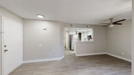 This single-floor residence offers a clean, modern aesthetic throughout, characterized by neutral warm-gray walls, light wood-look flooring, and textured ceilings that tie the space together cohesively. The open-concept layout connects the living area to the kitchen seamlessly, making the space feel airy and functional. The living area is generously proportioned, featuring a ceiling fan, a sliding glass door with vertical blinds that invites natural light, and a bright window that further illuminates the room. The kitchen is well-appointed with white cabinetry, light stone-look countertops, and stainless steel appliances including a refrigerator, electric range, and over-the-range microwave. A peninsula with a double stainless steel sink and additional counter space provides both extra prep area and a natural divide between the kitchen and living spaces. A skylight above the kitchen enhances the brightness of the cooking area. The bedroom is a comfortable, light-filled space with a window and a sliding mirrored closet door. The bathroom features a white vanity with stone-look countertops, white cabinetry with brushed nickel hardware, a large mirror, and a tub-shower combination, all finished in a clean, neutral palette. The unit's consistent flooring, crisp white trim, and modern fixtures give the entire space a refreshed, move-in-ready feel.