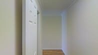 This single-floor space presents a clean and well-maintained interior with a cohesive design aesthetic throughout. The hallway immediately sets the tone, showcasing warm hardwood flooring that runs seamlessly underfoot, complemented by crisp white baseboards and elegant crown molding that lines the ceiling. The walls are finished in a soft, neutral tone that enhances the sense of brightness and openness, reflecting light evenly across the space. A classic six-panel white door with traditional hardware adds a timeless architectural detail, consistent with the overall refined yet understated character of the interior. The ceiling height provides a comfortable sense of volume, and the clean lines of the molding lend a polished, finished appearance to each area. The layout appears thoughtfully organized, with clear transitions between spaces. The neutral color palette and classic finishes create a versatile backdrop suitable for a variety of interior styles. Overall, the space exudes a quiet, functional elegance — characterized by careful attention to detail in its trim work, flooring, and overall finish quality — making it a well-appointed and move-in-ready environment.