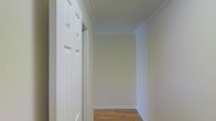 This single-floor space presents a clean and well-maintained interior with a cohesive design aesthetic throughout. The hallway immediately sets the tone, showcasing warm hardwood flooring that runs seamlessly underfoot, complemented by crisp white baseboards and elegant crown molding that lines the ceiling. The walls are finished in a soft, neutral tone that enhances the sense of brightness and openness, reflecting light evenly across the space. A classic six-panel white door with traditional hardware adds a timeless architectural detail, consistent with the overall refined yet understated character of the interior. The ceiling height provides a comfortable sense of volume, and the clean lines of the molding lend a polished, finished appearance to each area. The layout appears thoughtfully organized, with clear transitions between spaces. The neutral color palette and classic finishes create a versatile backdrop suitable for a variety of interior styles. Overall, the space exudes a quiet, functional elegance — characterized by careful attention to detail in its trim work, flooring, and overall finish quality — making it a well-appointed and move-in-ready environment.