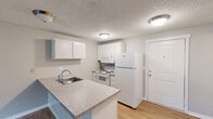 Located at 401 E Magnesium Rd in Spokane, WA, this one-bedroom, one-bathroom unit offers a practical and well-organized single-floor layout. The open-concept kitchen and living area form the heart of the unit, where light wood-style flooring in the kitchen transitions seamlessly into carpeted living space. The kitchen is equipped with white cabinetry, a full suite of white appliances including a refrigerator, electric range, and built-in microwave, along with a peninsula countertop featuring a granite-look surface and an integrated sink — ideal for casual dining or meal prep. The spacious living room is bright and airy, highlighted by a sliding glass door that opens onto a private balcony with outdoor views, and a textured ceiling throughout. Baseboard heating runs along the walls, ensuring comfort year-round. The bedroom offers a cozy carpeted retreat with a window overlooking the outdoors and a wall-mounted AC unit. Two doors from the bedroom lead to a hallway and a dedicated closet with shelving. The bathroom features light wood-style flooring, a full tub-shower combination, a vanity with a countertop sink, and a mirrored medicine cabinet, completing this functional and comfortable unit.