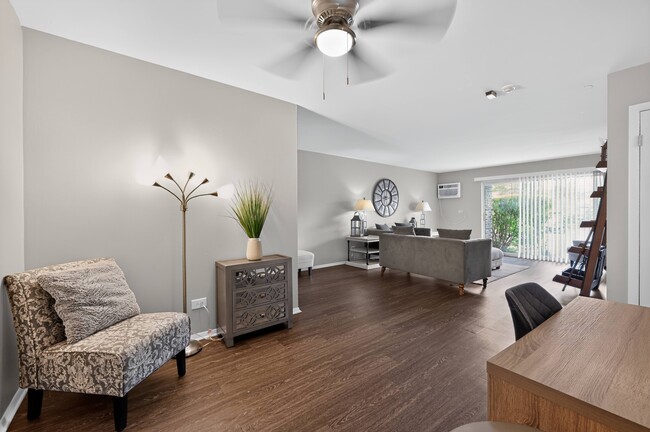 Relájese en una luminosa sala de estar con un sillón acogedor y plantas frescas en Renaissance at Carol Stream en Carol Stream, Illinois. - Renaissance at Carol Stream