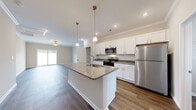 This well-designed single-story home offers a cohesive blend of modern finishes and functional layout throughout. The heart of the home is an open-concept kitchen that flows seamlessly into the living area, creating an inviting and spacious atmosphere. The kitchen is outfitted with crisp white shaker-style cabinetry, granite countertops, a classic subway tile backsplash, and a full suite of stainless steel appliances. A large central island with a built-in sink and pendant lighting above serves as both a practical workspace and a natural gathering point. Crown molding and recessed lighting add a refined touch to the main living areas, which also feature ceiling fans and large sliding glass doors that flood the space with natural light and provide outdoor access. Rich hardwood-style flooring runs consistently throughout the home, unifying each room with warmth and continuity. The bedrooms are generously proportioned, featuring neutral tones, natural window light, and ample closet space. The bathroom is cleanly finished with granite vanity countertops and a full shower-tub combination. A dedicated laundry room with wire shelving, washer and dryer hookups, and a pet door adds everyday convenience to this thoughtfully appointed home.