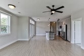 Located at 1441–1447 Commerce Dr in Decatur, GA, this single-floor unit offers a thoughtfully designed open-concept layout with contemporary finishes. Light wood-tone flooring runs throughout the main living areas, complementing neutral wall tones and crisp white baseboards to create a clean, modern aesthetic.

The living and dining area is generously sized, bathed in natural light from multiple large windows that frame views of surrounding greenery. Ceiling fans are installed throughout, enhancing comfort and airflow. The kitchen is a standout feature, equipped with stainless steel appliances including a range, microwave, and French door refrigerator. Light wood-grain cabinetry extends to the ceiling, paired with dark countertops, a subway tile backsplash, and a central island with built-in wine storage and pendant lighting above.

A hallway connects the main living space to the private quarters, featuring built-in wall niches for added character. Bedrooms are carpeted and well-lit with natural light from standard windows. The primary bathroom includes a dark-countered vanity, tile flooring, and access to a walk-in closet. A secondary bathroom features a soaking tub with a tiled surround and chrome fixtures, providing a clean and functional design throughout.
