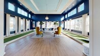 Located at 900 Owl Wood Lane in Summerville, SC, this single-story amenity center is designed with a coastal aesthetic that blends sophistication and comfort. The space is anchored by a striking game room with deep navy blue walls, soaring ceilings with a coffered sky-blue inset, and an abundance of natural light pouring in through tall windows on multiple sides. Two indoor putting greens and a bowling lane run along the perimeter of the room, while bold yellow wingback chairs and a central seating arrangement create an inviting social hub. Adjacent to the game room, a bright and airy lounge area features shiplap white walls, warm wood-look flooring, rattan pendant lighting, and a mix of navy and neutral seating arrangements, including a cozy media nook with built-in shelving, curated décor, and a wall-mounted television. The fully appointed kitchen showcases white cabinetry, a decorative herringbone tile backsplash, a tiled island with bar seating, pendant lighting with gold accents, a large flat-screen TV, and stainless steel appliances including a smart beverage dispenser. Throughout the space, warm hardwood-style flooring, shiplap paneling, and carefully curated coastal furnishings create a cohesive, welcoming atmosphere ideal for community gatherings and recreation.