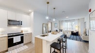 Located at 3 Executive Drive in Evesham, NJ, this well-appointed 2-bedroom, 3-bathroom residence offers a thoughtfully designed single-floor layout with a clean, contemporary aesthetic. The open-concept kitchen and living area serves as the heart of the home, anchored by a central island with a white quartz countertop, an undermount sink, and seating for two. Pendant globe lights with brass accents hang above the island, adding a warm, modern touch. The kitchen is outfitted with stainless steel appliances, two-tone cabinetry featuring white upper cabinets and light wood lower cabinets, and a classic white subway tile backsplash. Light-toned wood-style flooring runs throughout, enhancing the bright and airy feel. The living room receives generous natural light through large windows with views of surrounding trees, creating a welcoming, open atmosphere. Both bedrooms are comfortably sized, with the spacious primary bedroom offering ample room and large windows. The three bathrooms feature light wood vanities with white countertops, tile flooring, and glass-enclosed showers, maintaining the home's consistent modern palette. Crisp white walls and recessed lighting throughout contribute to a cohesive, polished living environment.
