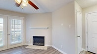 This one-bedroom, one-bathroom unit in Little Rock, Arkansas offers a practical and well-appointed layout across a single floor. The combined kitchen and living area forms the heart of the space, where wood-style laminate flooring runs throughout. The living room is highlighted by a fireplace with a clean white mantel shelf, a ceiling fan with light fixture, and French doors that invite natural light and provide outdoor access. The kitchen is equipped with dark cabinetry contrasting against light countertops, white appliances including a refrigerator, range, microwave, and dishwasher, and a peninsula with a sink that opens toward the living area. A skylight panel above the kitchen adds additional brightness. The bedroom features plush carpeting, a ceiling fan, and a large window with views of surrounding trees, creating a calm and naturally lit retreat. A closet door is visible, offering dedicated storage. The bathroom includes a full tub-shower combination with large-format tile surround and wood-style flooring. Neutral tones and clean finishes throughout give the space a cohesive, move-in ready appearance well-suited for comfortable single-occupant or couple living.