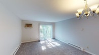 This single-floor residence at 4467 Colerain Ave in Cincinnati, Ohio offers a straightforward, functional layout across several well-defined living spaces. The main living area is generously proportioned, featuring neutral gray carpet, light-toned walls, and a sliding glass door fitted with vertical blinds that invites natural light and provides outdoor views. A wall-mounted air conditioning unit and baseboard heating ensure year-round comfort. An adjoining area, illuminated by an elegant chandelier, flows openly toward the kitchen and additional rooms, creating a connected and airy feel throughout.

The kitchen is equipped with warm oak cabinetry extending to the upper and lower walls, light laminate countertops, a double stainless steel sink, and a black electric range, offering practical storage and workspace. A separate bedroom features plush carpeting, a window overlooking greenery, a ceiling light fixture, and baseboard heating. Closet space is visible from the main living area, adding to the unit's organizational convenience. The bathroom includes a full tub and shower combination with clean white surround panels and chrome fixtures. Overall, the space presents a clean, understated aesthetic well-suited for comfortable everyday living.