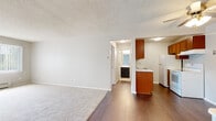 This single-floor unit offers a clean, functional layout designed for comfortable everyday living. The open living and dining area serves as the heart of the space, featuring a combination of rich dark hardwood-style flooring and soft wall-to-wall carpeting, along with a ceiling fan and a large window that invites natural light and creates an airy atmosphere. A baseboard heating system ensures year-round comfort.

The kitchen is efficiently designed and positioned adjacent to the living area, equipped with warm medium-toned wood cabinetry, light-colored countertops, a double sink, a full-size refrigerator, and a freestanding electric range with an overhead vent hood — providing all the essentials for everyday meal preparation.

The bedrooms are generously proportioned, each finished with plush wall-to-wall carpeting and neutral-toned walls that create a calm, restful environment. One bedroom features a ceiling fan and window with natural light, while another offers a quiet, softly lit retreat.

The bathroom is finished with clean white square tile surrounding a full soaking tub and shower combo, complemented by mosaic tile flooring, a white vanity with a dark cabinet base, and simple, timeless fixtures. A hallway connects the rooms, completing this practical and move-in-ready layout.