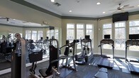 Located in Morrisville, NC, this fitness center offers a thoughtfully designed, single-floor workout facility built to support a comprehensive exercise routine. The space is bright and open, benefiting from an abundance of large, white-framed windows that flood the room with natural light and provide views of the surrounding outdoor greenery. Recessed ceiling lights supplement the natural illumination, ensuring the space remains well-lit throughout the day. Crown molding along the ceiling adds a polished architectural detail that elevates the overall aesthetic.

A full-length mirrored wall on one side visually expands the room while allowing users to monitor their form during workouts. The fitness area is equipped with a variety of strength-training machines, including a multi-function cable and weight machine as well as a chest press unit, catering to targeted muscle group training. For cardiovascular exercise, the space features treadmills and an elliptical trainer, each equipped with individual display screens. Rubber floor matting is positioned beneath the equipment to provide safety and stability. The neutral, warm-toned walls and carpeted perimeter contribute to a clean, welcoming atmosphere that makes this fitness center both functional and comfortable for daily use.