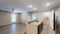 This single-story residence is designed with an open-concept layout that connects the kitchen and living areas into one cohesive, functional space. The kitchen serves as a central focal point, featuring a peninsula with granite countertops and an undermount sink, dark cabinetry, stainless steel appliances including a side-by-side refrigerator, and recessed lighting overhead. The countertop overhang provides a convenient breakfast bar arrangement that flows naturally into the living area.

The living space is generously proportioned, finished with wood-style luxury vinyl plank flooring that runs consistently throughout the unit. Neutral beige tones on the walls complement the light flooring, creating a bright and clean aesthetic. Ceiling fans are installed in the main living areas, enhancing air circulation and comfort.

The bedroom is a well-sized room with its own ceiling fan, a window for natural light, and a dedicated closet with a rod and shelving system. The full bathroom includes a tub-shower combination with tile surround, a dark-cabineted vanity with a granite countertop and single sink, and wood-style flooring. A dedicated laundry alcove with washer and dryer hookups adds practical convenience to the layout.