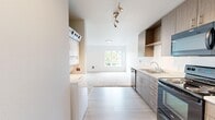 This studio located on 53rd Ave S in Seattle, WA, offers a thoughtfully designed single-floor layout that maximizes functionality within a compact footprint. The open-concept design seamlessly connects the kitchen and living area, creating an efficient and cohesive living space.

The kitchen is a standout feature, equipped with medium-toned wood grain cabinetry offering ample upper and lower storage, open shelving, light-colored countertops, and a full suite of stainless steel appliances including an electric range, microwave, dishwasher, and refrigerator. A single-basin sink with modern fixtures completes the practical setup. Light wood-look flooring runs through the kitchen, transitioning into plush carpeting in the living area.

The living space is bright and open, with a large window framing views of surrounding greenery, allowing natural light to fill the room. White walls and clean lines maintain a crisp, contemporary aesthetic throughout.

The bathroom features wood-toned cabinetry with a vanity and sink, light wood-look flooring, and a clean, minimal design. An in-unit stacked washer and dryer adds everyday convenience. Track lighting in the kitchen and ample natural light throughout give the studio a modern, well-lit ambiance.