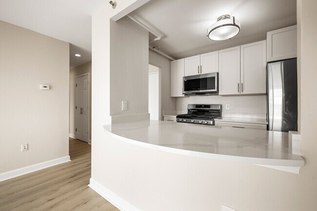 Cocina moderna con elegantes encimeras de cuarzo Statuario, gabinetes blancos, electrodomésticos de acero inoxidable y estufa de gas para un aspecto sofisticado en Parkside Place, apartamentos en Cambridge, MA. - Parkside Place