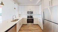 Located in Homestead, FL, this thoughtfully designed 2-bedroom, 1-bathroom unit offers a clean, modern aesthetic throughout. The open-concept kitchen and living area anchors the space, featuring sleek white cabinetry extending to the ceiling, stainless steel appliances including a range, microwave, dishwasher, and refrigerator, and a white quartz countertop with an integrated sink. Warm wood-look flooring flows throughout the unit, complementing the bright, white walls and recessed lighting. A peninsula counter adds workspace and visual separation between the kitchen and living area.

The primary bedroom is a standout, boasting floor-to-ceiling sliding glass doors and expansive windows that open to a private balcony with scenic outdoor views, allowing abundant natural light and a refreshing sense of openness. A ceiling fan adds comfort to the room. The second bedroom also benefits from natural light, with dual windows offering outdoor views and a ceiling fan overhead.

The bathroom is cleanly finished in white tile, featuring a combination tub and shower with a curved curtain rod, a vanity, and modern fixtures. A hallway connects the rooms, maintaining a practical and efficient layout. Throughout the unit, the consistent use of neutral tones and contemporary finishes creates a cohesive, move-in-ready living environment.