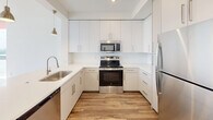 Located in Homestead, FL, this thoughtfully designed 2-bedroom, 1-bathroom unit offers a clean, modern aesthetic throughout. The open-concept kitchen and living area anchors the space, featuring sleek white cabinetry extending to the ceiling, stainless steel appliances including a range, microwave, dishwasher, and refrigerator, and a white quartz countertop with an integrated sink. Warm wood-look flooring flows throughout the unit, complementing the bright, white walls and recessed lighting. A peninsula counter adds workspace and visual separation between the kitchen and living area.

The primary bedroom is a standout, boasting floor-to-ceiling sliding glass doors and expansive windows that open to a private balcony with scenic outdoor views, allowing abundant natural light and a refreshing sense of openness. A ceiling fan adds comfort to the room. The second bedroom also benefits from natural light, with dual windows offering outdoor views and a ceiling fan overhead.

The bathroom is cleanly finished in white tile, featuring a combination tub and shower with a curved curtain rod, a vanity, and modern fixtures. A hallway connects the rooms, maintaining a practical and efficient layout. Throughout the unit, the consistent use of neutral tones and contemporary finishes creates a cohesive, move-in-ready living environment.