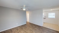 This single-floor space offers a well-organized and functional layout designed for comfortable living. The main living area is bright and open, featuring warm wood-look laminate flooring, soft neutral gray walls, and a ceiling fan with integrated lighting. Multiple windows dressed with horizontal blinds allow natural light to fill the room, creating an airy atmosphere. The space flows seamlessly toward a dedicated kitchen area, which is fitted with white cabinetry, a dark countertop, a double-basin stainless steel sink, white appliances, and a tile backsplash. Tile flooring in the kitchen provides a practical transition from the wood-look floors in the living spaces. The bedrooms continue the consistent design language, each offering wood-look flooring, ceiling fans, neutral-toned walls, and windows that bring in natural light. The bathroom is cleanly finished with light tile flooring, a full tub-shower combination, and a window for ventilation and natural light. Throughout the space, clean white trim, textured ceilings, and a cohesive neutral color palette contribute to a tidy, move-in-ready aesthetic that is both practical and welcoming.