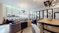 Located at 1916 Addison Street in the heart of Berkeley, California, this single-floor leasing office and amenity lounge is a study in contemporary design and functional elegance. Large street-facing windows flood the open main area with natural light, offering views of the surrounding urban landscape while bold, sculptural pendant light fixtures — featuring multi-bulb, globe-style chandeliers — serve as eye-catching focal points overhead.

The main lounge area is thoughtfully arranged with a variety of seating configurations, including plush navy and charcoal sofas, cane-back chairs, and round side tables, creating an inviting and versatile environment. A large communal wood-top dining table anchors one side of the space, ideal for meetings or collaborative gatherings. The floor features a striking geometric tile pattern in contrasting light and dark tones that adds visual depth and dimension throughout.

A glass-enclosed room with sleek black-framed floor-to-ceiling doors provides a semi-private lounge or meeting area, furnished with a sofa, television, and gallery wall, while remaining visually connected to the main space. A dedicated multi-purpose room is marked by a sophisticated built-in dark wood shelving unit displaying curated books and decorative objects. An adjacent hall features bold vertical tile detailing and an ornamental metal railing, adding architectural interest and a polished, gallery-like quality to the overall space.