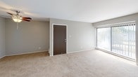 Located at 212 Gladstone Dr in Glendale Heights, Illinois, this single-floor residence offers a well-organized and functional layout. The spacious living room is finished with neutral-toned carpet and features a ceiling fan with light fixture, a large sliding glass door that fills the space with natural light, and direct access to an outdoor balcony deck. The open layout connects seamlessly to the kitchen, which is equipped with rich dark-wood cabinetry, black appliances including an electric range, built-in microwave, and dishwasher, complemented by a double-basin sink and light tile flooring. A sliding glass door in the kitchen also provides views and access to the balcony. The bedrooms are carpeted and feature neutral gray walls, baseboard heating, and windows with blinds that bring in natural light and exterior views. One bedroom includes a bifold closet with built-in shelving. The bathroom is well-appointed with full-wall stone-look tile surrounding a soaking tub and shower combination, a curved curtain rod, tile flooring, and brushed nickel fixtures. Throughout the space, a consistent neutral color palette and clean finishes create a calm, cohesive atmosphere.