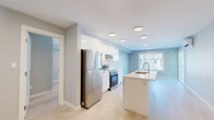 This single-floor residence offers a thoughtfully designed layout across two bedrooms and two bathrooms. The open-concept kitchen and living area serves as the heart of the unit, featuring a central island with an integrated sink, stainless steel appliances including a refrigerator and electric range, and high-gloss white cabinetry. Light hardwood-style flooring runs throughout, complementing the soft blue-grey walls and bright, recessed ceiling lighting that collectively create an airy, modern ambiance. Natural light enters through windows fitted with horizontal blinds, enhancing the sense of openness.

The primary bedroom is a comfortable size, equipped with a stylish sliding barn door that opens to a dedicated closet. The second bedroom features its own window with natural light and a baseboard heater. Both rooms continue the consistent light flooring and neutral wall tones found throughout the unit.

The two bathrooms are finished in a clean, contemporary style. One includes a full soaker tub with a tiled surround and a white vanity with an integrated countertop, while the second features a glass-enclosed walk-in shower. Both bathrooms maintain a cohesive, minimalist aesthetic with neutral tile flooring and recessed lighting.