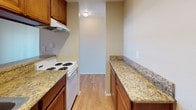 This single-floor unit at 532 Broadway in El Cajon, California offers a well-designed layout with comfortable living spaces throughout. The open living and dining area is finished with plush carpeting and features a ceiling fan overhead, creating a relaxed and functional environment. A half-wall pass-through with a granite countertop connects the living space to the kitchen, which is outfitted in a galley configuration with warm wood cabinetry, granite countertops along both sides, a white range, and a vent hood. The light wood flooring in the kitchen adds a clean contrast to the surrounding neutral tones. A spacious carpeted room features a sliding glass door that opens to a private balcony, allowing natural light to fill the space and offering outdoor views of the surrounding area. Vertical blinds provide privacy and light control. The bathroom is thoughtfully appointed with a rich wood vanity topped with granite, a large mirror with Hollywood-style lighting, and an adjacent shower. Neutral wall tones are consistent throughout the unit, contributing to a cohesive and move-in-ready ambiance. This residence combines practical finishes with comfortable design in a convenient El Cajon location.