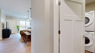 Located at 3800 Jeffers Pky NW in Prior Lake, MN, this well-appointed one-bedroom, one-bathroom residence offers a thoughtfully designed single-floor layout that maximizes every square foot. The living room serves as the heart of the home, featuring warm hardwood-style flooring, crown molding, and a large sliding glass door that opens to a private balcony, filling the space with natural light and offering pleasant outdoor views. The kitchen is a standout, showcasing rich walnut cabinetry, stainless steel appliances including a refrigerator, range, and microwave, light countertops, and a center island with seating for three — finished with stylish pendant lighting overhead. The bedroom is a comfortable retreat with plush carpeting, a spacious walk-in closet, and a serene, neutral color palette. A dedicated office nook with carpeted flooring provides a quiet workspace. The bathroom features a full tub-shower combination with wood-toned vanity cabinetry and hardwood-style flooring. A separate laundry area includes a stacked washer and dryer unit along with built-in wire shelving for added storage. Throughout the residence, a cohesive neutral tone and modern finishes create a clean, inviting ambiance.